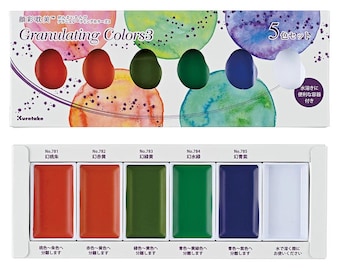 Puede incluir: Un juego de pintura de acuarela etiquetado como "Granulating Colors 3" con cinco colores: rojo, naranja, verde, azul y blanco. El juego incluye un recipiente para mezclar e instrucciones en japonés. Cada color está en una pastilla rectangular.