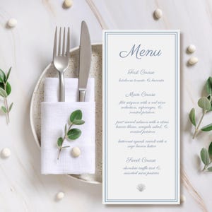 May include: A formal menu card with a blue border and elegant script. The menu lists a multi-course meal, including filet mignon and butternut squash ravioli. A fork and knife rest on a white napkin, with greenery and decorative elements.