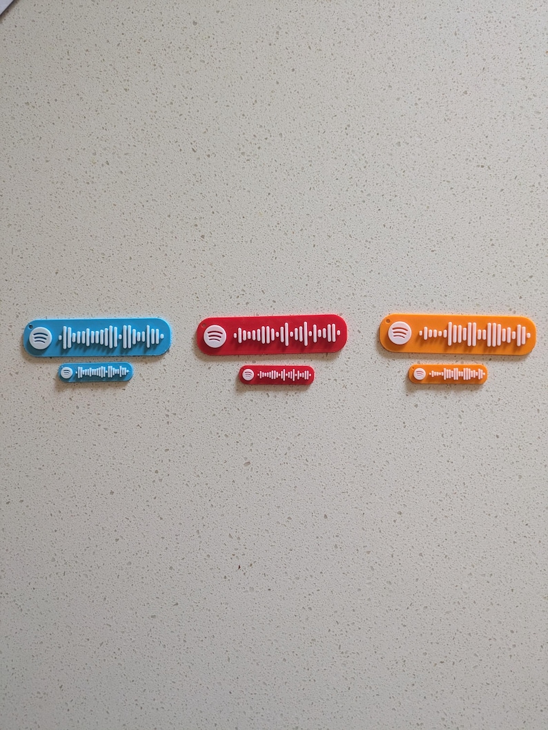 May include: Three colorful Spotify code plaques in blue, red, and orange, each with a matching smaller version. The plaques feature the Spotify logo and a series of vertical lines representing a unique audio track.