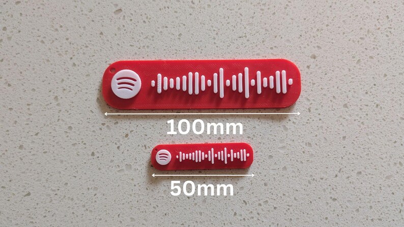 May include: Two red Spotify code tags, one 100mm long and the other 50mm long. Both tags have a white Spotify logo and a white sound wave pattern. The tags are on a light gray speckled surface.