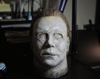 Puede incluir: Una taza de cerámica blanca con un asa negra y el texto "But First, Coffee" en un estilo manuscrito. La taza está sobre una superficie blanca. La taza mide aproximadamente 10 cm de alto.