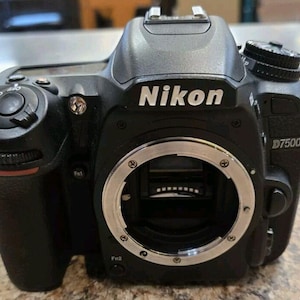 May include: Black Nikon D7500 digital SLR camera. The camera body features the Nikon logo in white, a lens mount, and various control dials and buttons. The model number D7500 is visible on the side.
