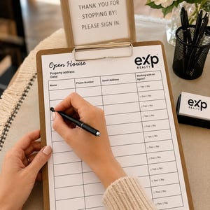 May include: A brown wooden clipboard holding an eXp Realty open house sign-in sheet with columns for name, phone number, email address, and agent status. A black pen is held over the paper. A welcome sign and a black pen holder are nearby.