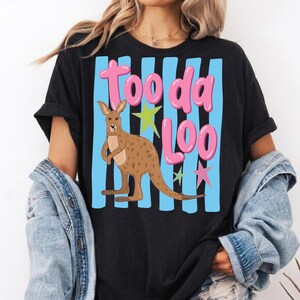Może przedstawiać: Czarny t-shirt z kresk&oacute;wkowym kangurem i napisem "Tooda Loo" w r&oacute;żowych literach bąbelkowych. Kangur jest brązowy, na tle niebieskich pionowych pask&oacute;w i kolorowych gwiazd.