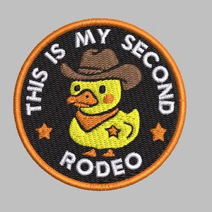 May include: Circular embroidered patch with a yellow duck wearing a cowboy hat and bandana. The patch has the text "THIS IS MY SECOND RODEO" in white. The border is orange with two orange stars.