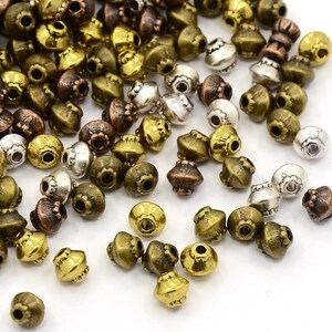 May include: A large assortment of antique gold, silver, and bronze metal beads. The beads are all in the shape of a small, rounded cone with a hole at the top. The beads are perfect for jewellery making or other craft projects.