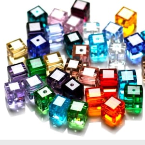May include: Assortment of colorful square glass beads. The beads are in various colors, including red, orange, yellow, green, blue, purple, and clear. The beads are all the same size and shape.