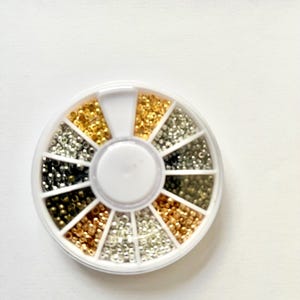 May include: A white plastic wheel with 12 compartments filled with small gold, silver, and black beads.