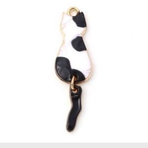 May include: A gold charm with a black and white enamel cat design. The cat is facing away from the viewer and has a dangling tail.