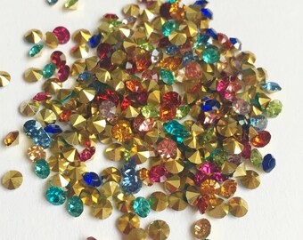 May include: A large pile of colorful rhinestones, mostly gold, with a variety of colors including red, blue, green, and purple.