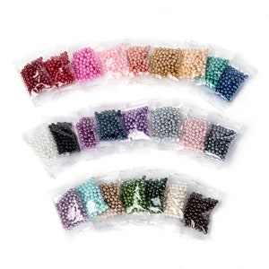 May include: Assortment of small pearl beads in various colors, packaged in individual clear plastic bags. The beads are arranged in a semi-circle pattern.