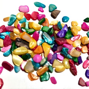 May include: A collection of colourful, iridescent, and natural shell pieces in various shapes and sizes. The shells are a mix of pink, blue, green, yellow, and brown.