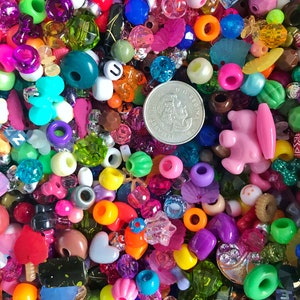 May include: A large assortment of colorful plastic beads in various shapes and sizes, including letters, hearts, stars, and smiley faces. A Canadian coin is included in the mix.