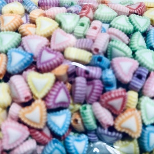 Peut inclure: Gros plan sur un tas de perles en forme de cœur colorées. Les perles sont en plastique et ont un centre blanc avec une bordure rayée colorée.