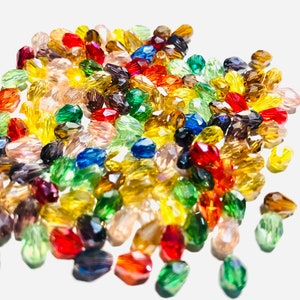 May include: A large assortment of colorful faceted glass beads in various shades of red, orange, yellow, green, blue, and purple. The beads are oval shaped and have a glossy finish.