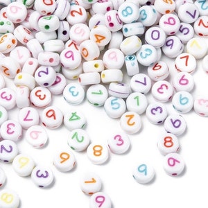 May include: A collection of white plastic beads with colorful numbers printed on them. The beads are scattered on a white surface.