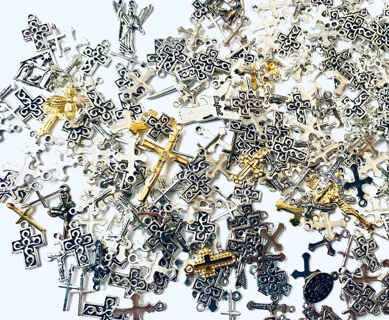 May include: A large collection of silver and gold cross charms. The charms are of various sizes and designs, with some featuring intricate details.