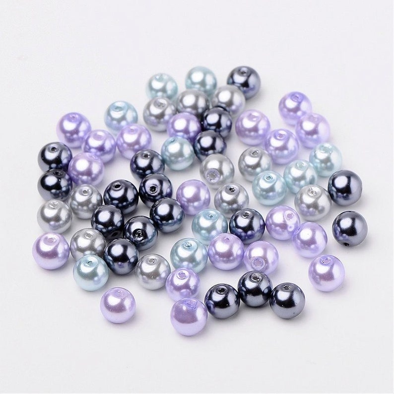 May include: A collection of pearl beads in shades of lavender, blue, and gray. The beads are round and have a smooth, glossy finish.
