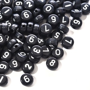 May include: A pile of black plastic beads with white numbers from 0 to 9. The beads are scattered on a white surface.