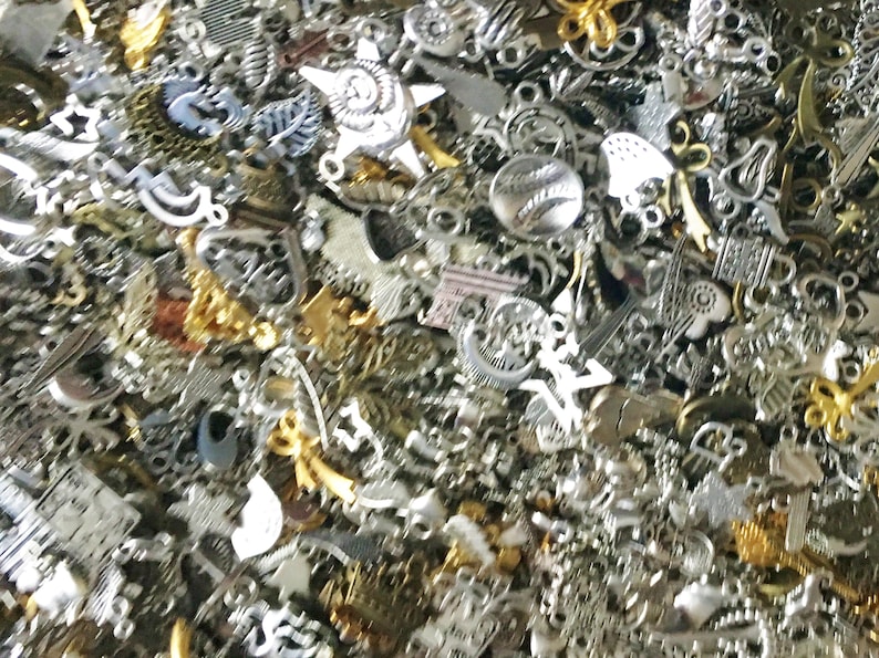 Puede incluir: Un gran surtido de abalorios de metal plateado y dorado. Los abalorios son de diversas formas y tama&ntilde;os, incluyendo corazones, estrellas y flores.