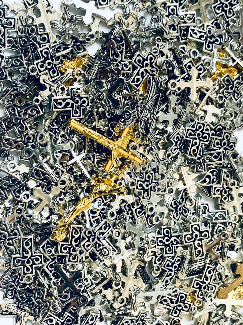 May include: A large pile of silver and gold cross charms. The charms are all different shapes and sizes, and some have intricate designs.