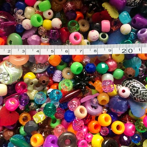 May include: A large assortment of colorful plastic beads, including round, square, and star shapes. The beads are arranged in a random pattern and are measured with a ruler.