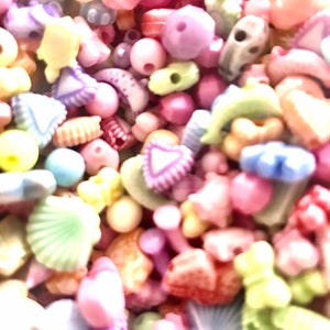May include: A large assortment of colorful plastic beads in various shapes, including hearts, stars, shells, and flowers. The beads are perfect for crafting jewelry, making hair accessories, or adding a touch of whimsy to any project.