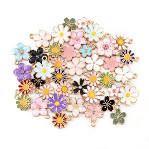Puede incluir: Surtido de abalorios de flores de esmalte de colores con detalles en tono dorado. Los abalorios presentan varios dise&ntilde;os de flores, incluyendo margaritas, flores de cerezo y otros patrones florales. Cada abalorio tiene un bucle para sujetarlo a joyas u otras manualidades.