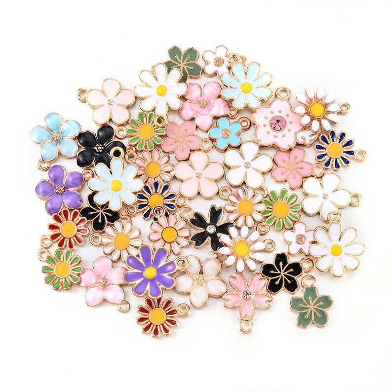 Puede incluir: Surtido de abalorios de flores de esmalte de colores con detalles en tono dorado. Los abalorios presentan varios dise&ntilde;os de flores, incluyendo margaritas, flores de cerezo y otros patrones florales. Cada abalorio tiene un bucle para sujetarlo a joyas u otras manualidades.