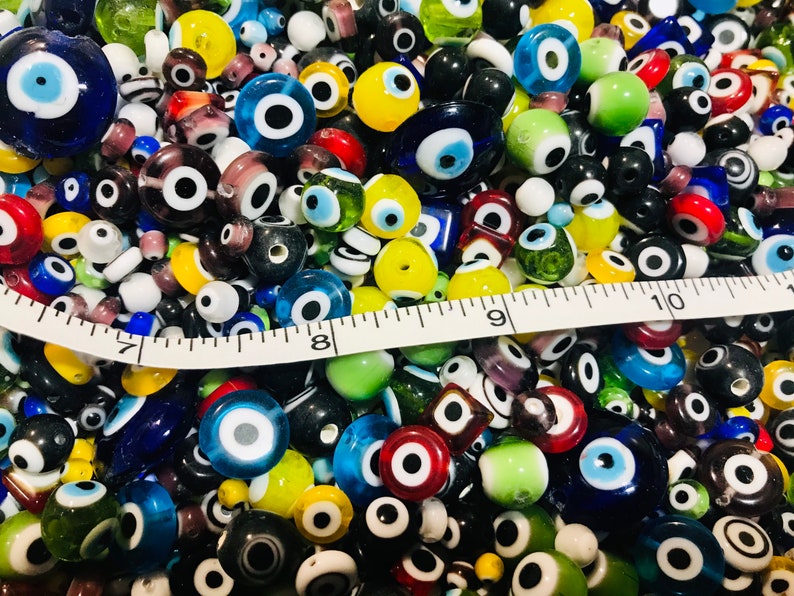 Pu&ograve; includere: Una grande collezione di perline di vetro colorate con un design di occhio turco. Le perline sono di varie forme e dimensioni, tra cui rotonde, ovali e quadrate. Le perline sono un mix di blu, verde, giallo, rosso e bianco.