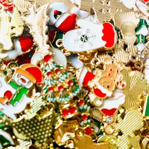 May include: A large assortment of gold-tone metal Christmas charms with various designs, including snowmen, reindeer, mittens, Christmas trees, and ornaments. The charms are decorated with red, green, and white enamel paint.
