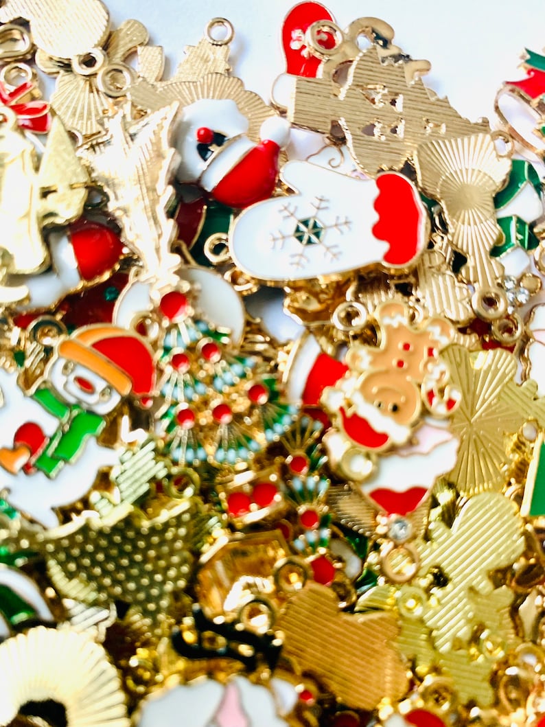 May include: A large assortment of gold-tone metal Christmas charms with various designs, including snowmen, reindeer, mittens, Christmas trees, and ornaments. The charms are decorated with red, green, and white enamel paint.