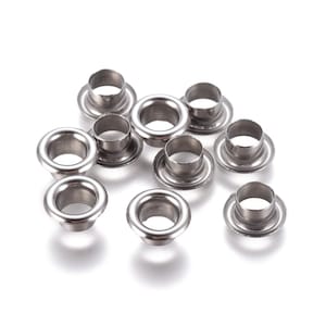May include: A close-up of ten silver metal eyelets, commonly used for crafts and leatherwork.