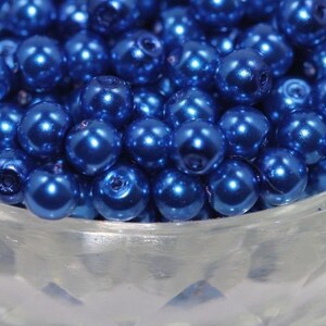 May include: A bowl filled with shiny, metallic blue round beads. The beads are smooth and have a pearlescent finish.