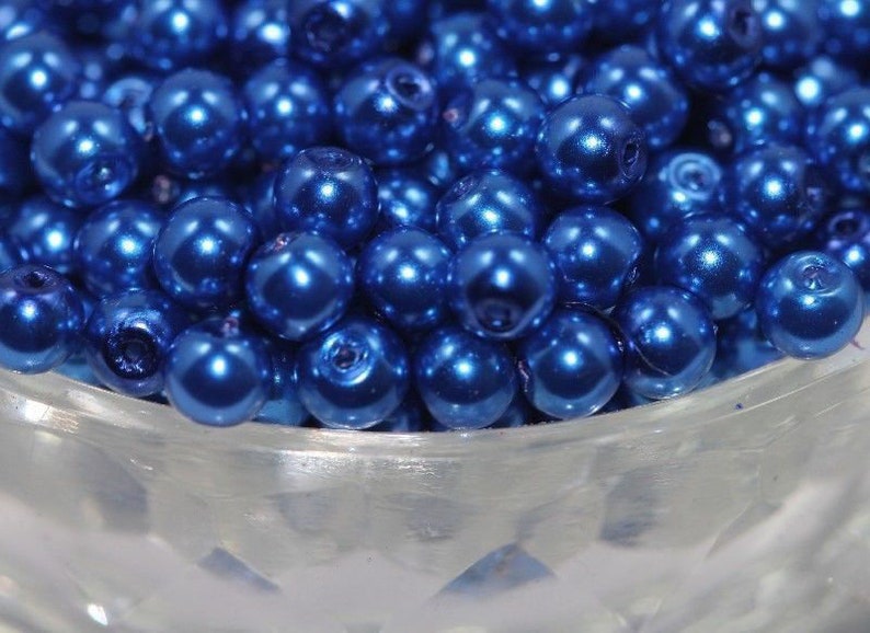 May include: A bowl filled with shiny, metallic blue round beads. The beads are smooth and have a pearlescent finish.