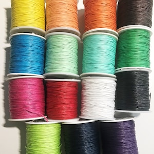 May include: Assortment of 14 spools of waxed cotton cord in various colours, including yellow, orange, blue, green, pink, red, white, black, and purple. The spools are arranged in a semi-circle on a white surface.