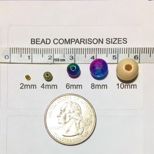 May include: A ruler with measurements in inches and centimeters, showing the size of different beads. The beads are 2mm, 4mm, 6mm, 8mm, and 10mm in diameter. The beads are made of different materials, including wood, metal, and glass. The beads are arranged in order of size, with the smallest bead on the left and the largest bead on the right. A US quarter is shown for size comparison.