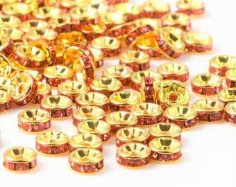 May include: A close-up of a pile of gold-toned metal bead caps with red rhinestone accents. The bead caps are round and have a small hole in the center.