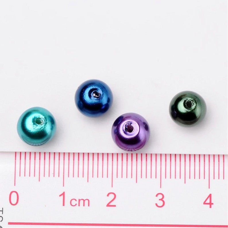 May include: Four round iridescent beads in different colors: teal, blue, purple, and green. The beads are about 1 cm in diameter and have a hole in the center.