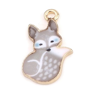 Op de afbeelding: Een gouden hanger met een grijze en witte vos met blauwe ogen. De hanger heeft een lus aan de bovenkant om aan een ketting of armband te bevestigen.