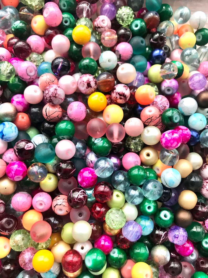 May include: A large assortment of colorful round beads in various shades of pink, green, blue, yellow, red, and purple. The beads are made of glass and have a variety of finishes, including matte, glossy, and iridescent.