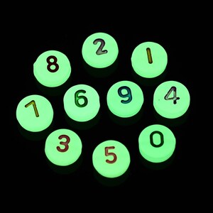 May include: Ten glow-in-the-dark round counters with numbers 0 through 9 printed on them. The counters are white with black numbers.