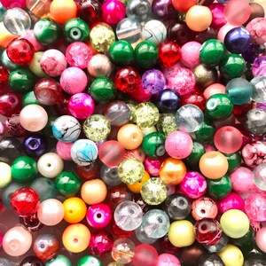 May include: A large assortment of colorful glass beads in various shapes and sizes. The beads are a mix of opaque and translucent colors, including red, green, blue, pink, yellow, and white.