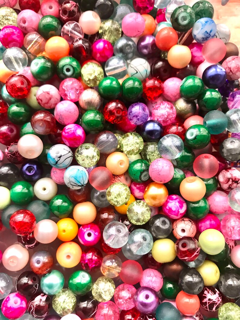 May include: A large assortment of colorful glass beads in various shapes and sizes. The beads are a mix of opaque and translucent colors, including red, green, blue, pink, yellow, and white.