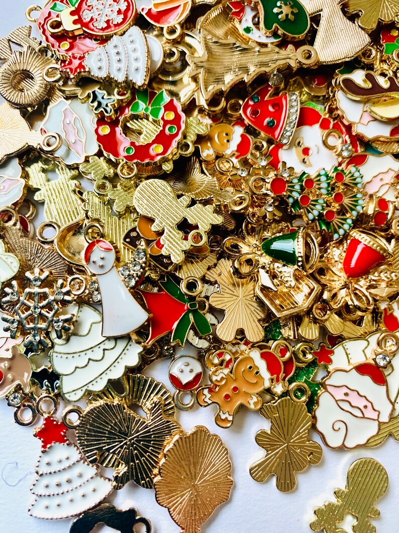 May include: A large assortment of gold-colored metal charms with various Christmas-themed designs. The charms feature a variety of colors, including red, green, white, and blue. Some of the charms are shaped like snowflakes, Christmas trees, bells, and Santa Claus.