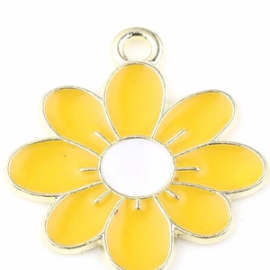 Puede incluir: Un dije de metal dorado en forma de flor amarilla con un centro blanco. La flor tiene seis p&eacute;talos y un bucle en la parte superior para sujetarlo a un collar o pulsera.