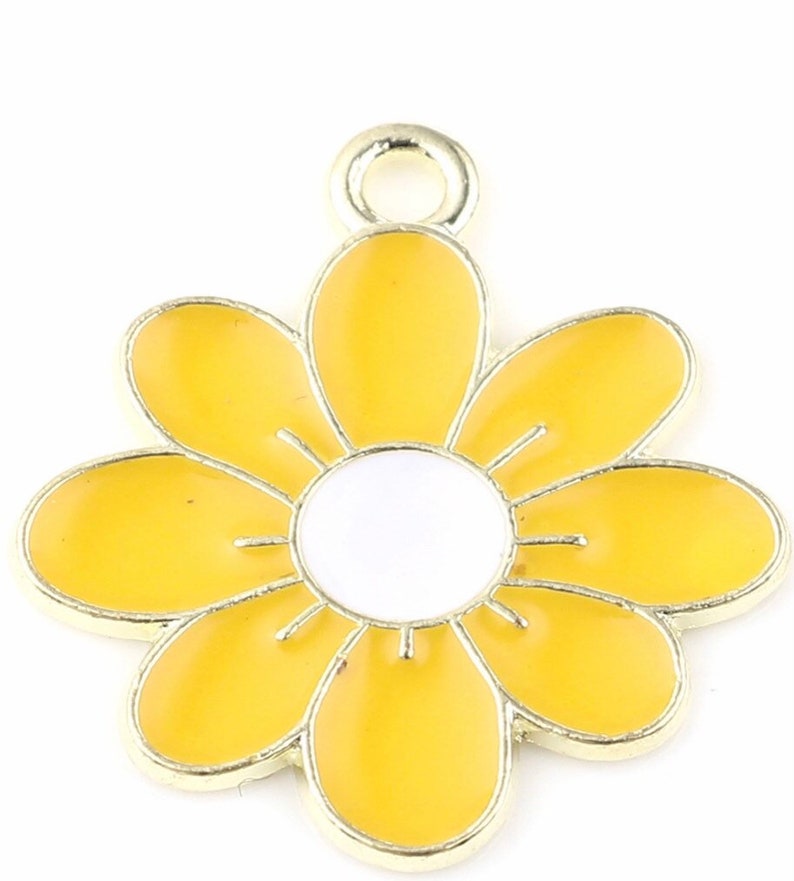 Puede incluir: Un dije de metal dorado en forma de flor amarilla con un centro blanco. La flor tiene seis p&eacute;talos y un bucle en la parte superior para sujetarlo a un collar o pulsera.