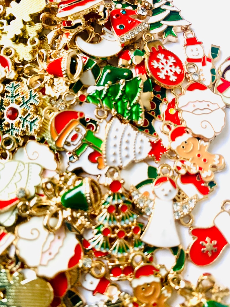 May include: Assortment of gold-tone Christmas charms with enamel details. The charms feature various holiday themes, including snowmen, Christmas trees, ornaments, and Santa Claus.