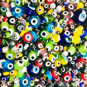 Pu&ograve; includere: Una vista ravvicinata di una variet&agrave; di perline di vetro blu maleocchio colorate. Le perline sono di varie forme e dimensioni, alcune con un solo occhio e altre con pi&ugrave; occhi. Le perline sono un mix di blu, verde, giallo, rosso e bianco.