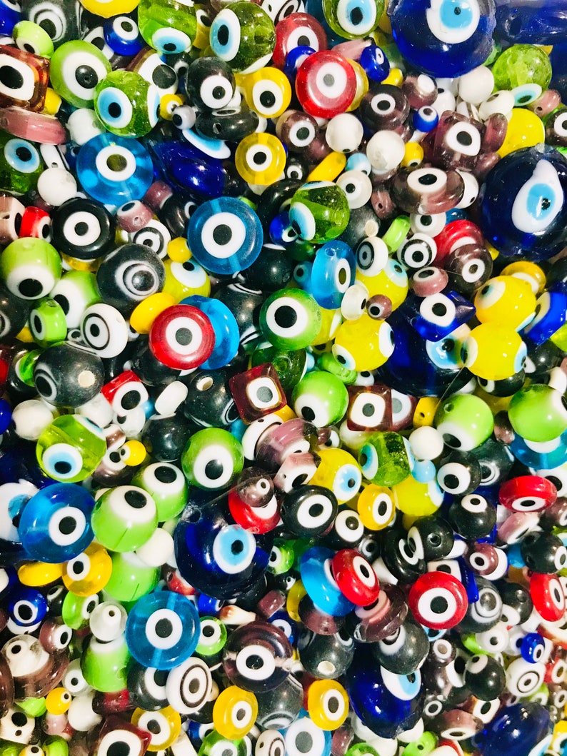 Pu&ograve; includere: Una vista ravvicinata di una variet&agrave; di perline di vetro blu maleocchio colorate. Le perline sono di varie forme e dimensioni, alcune con un solo occhio e altre con pi&ugrave; occhi. Le perline sono un mix di blu, verde, giallo, rosso e bianco.